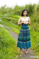 Miyuki Fukatsu standing on path outdoors pulling dress down revealing her small breasts